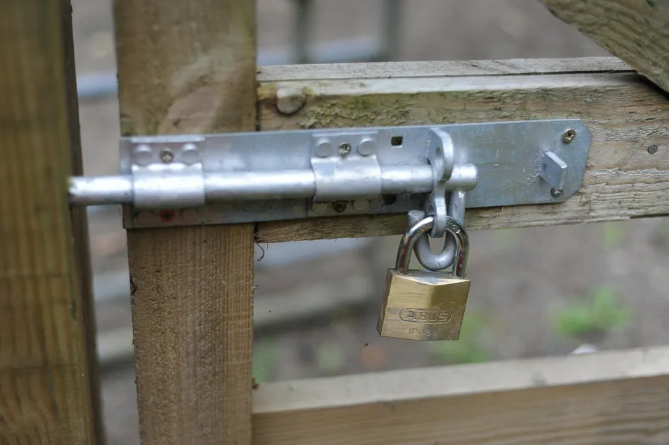 Close-up of a galvanized slide bolt latch with a brass padlock on a weathered wooden gate