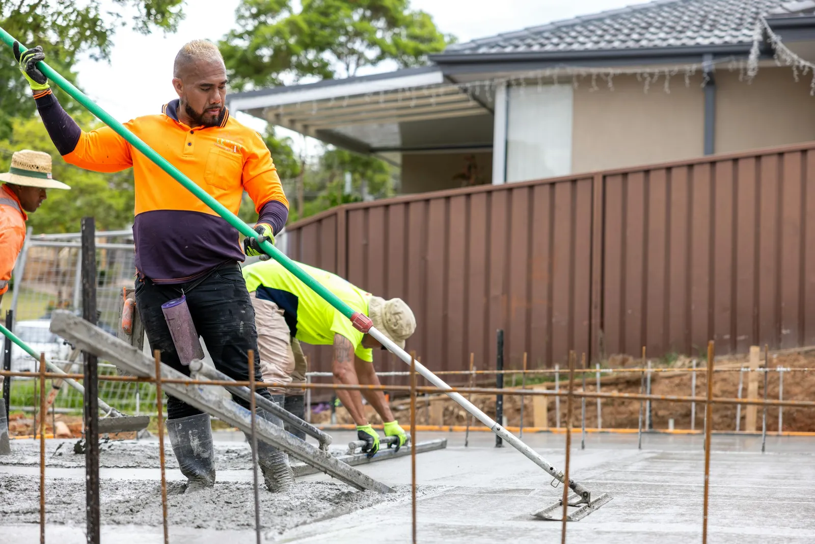 Two workers screeding a freshly poured concrete slab over rebar