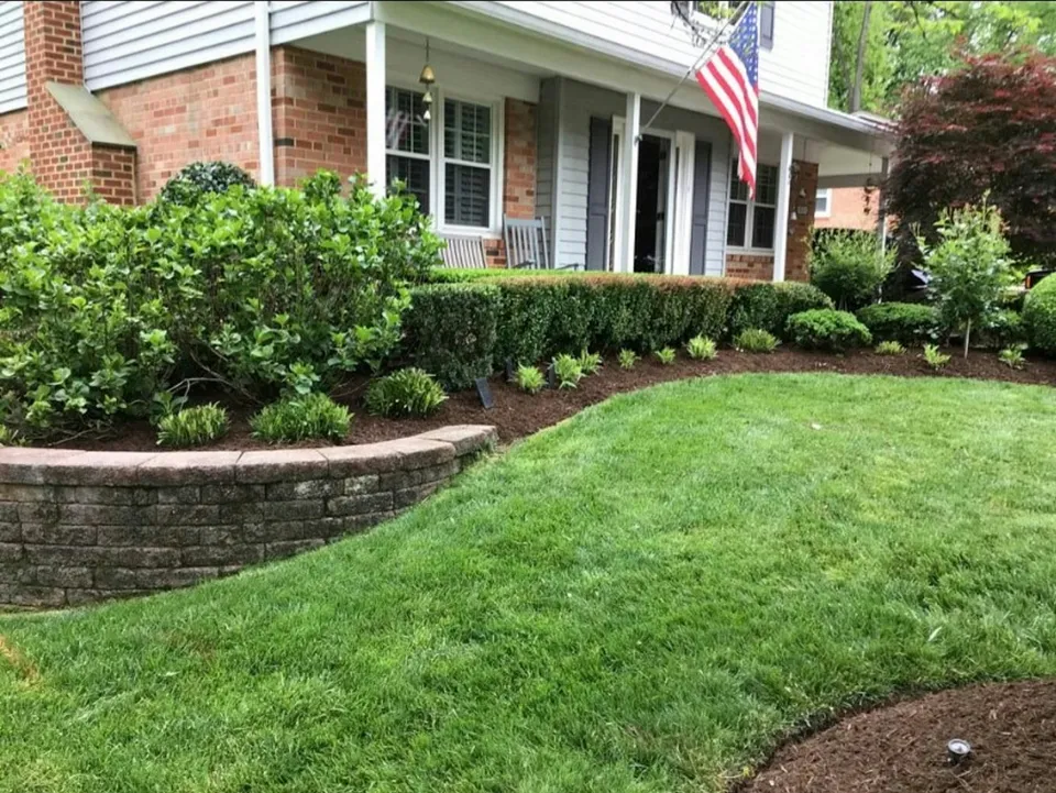 A front yard with a curved stone bed of shrubs and fresh mulch above a green lawn