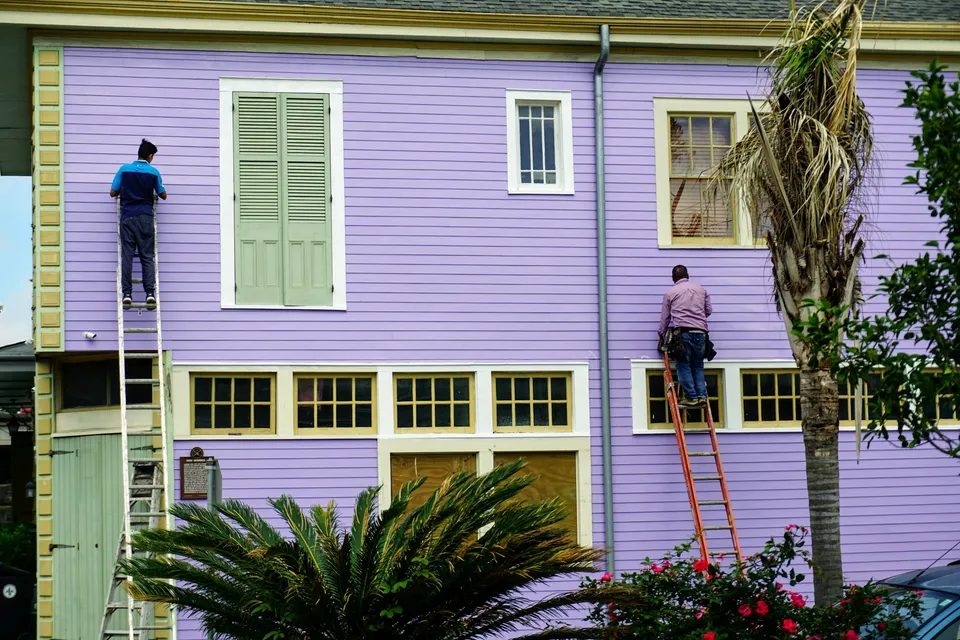 Two painters on ladders painting a two-story lavender clapboard house